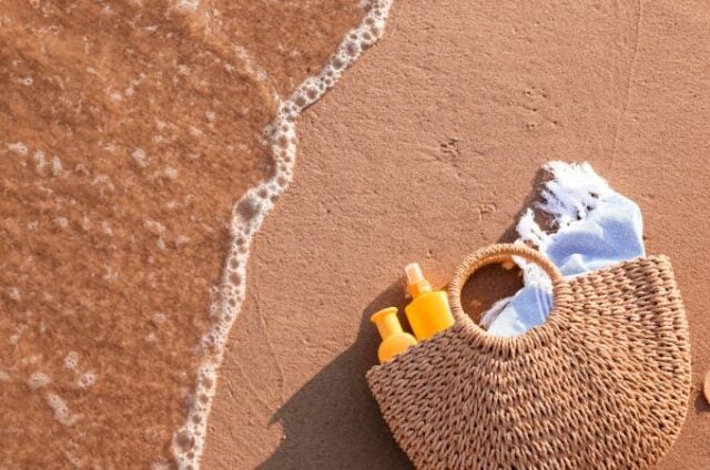 sunscreen and towel in beach basket at ocean